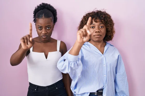 指を上げて怒りの表情でピンクの背景に立っている2人のアフリカの女性は ジェスチャーを示していません — ストック写真