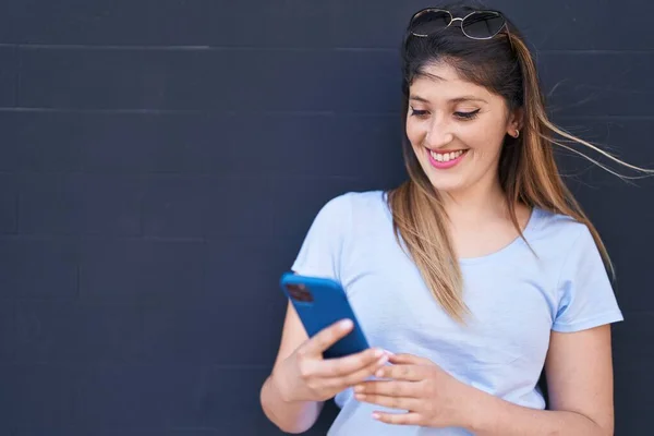 若いヒスパニック系の女性は黒の背景にスマートフォンを使用して自信を笑顔 — ストック写真