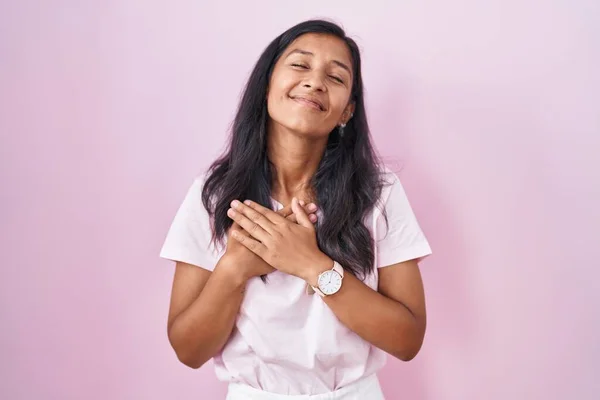 目を閉じて胸の上で手を笑顔ピンクの背景に立っている若いヒスパニック系の女性と顔に感謝のジェスチャー 健康の概念 — ストック写真