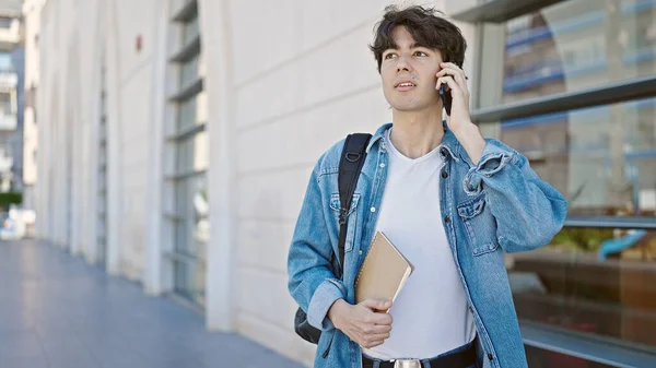若いヒスパニック系の男学生が大学で真剣な表情でスマートフォンで話しています — ストック写真