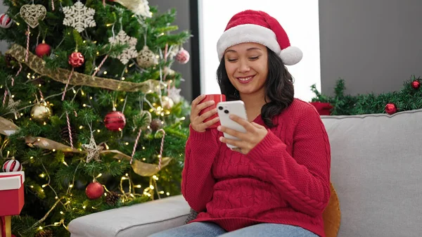 Νεαρή Όμορφη Ισπανόφωνη Γυναίκα Χρησιμοποιώντας Smartphone Πίνοντας Καφέ Γιορτάζοντας Χριστούγεννα — Φωτογραφία Αρχείου