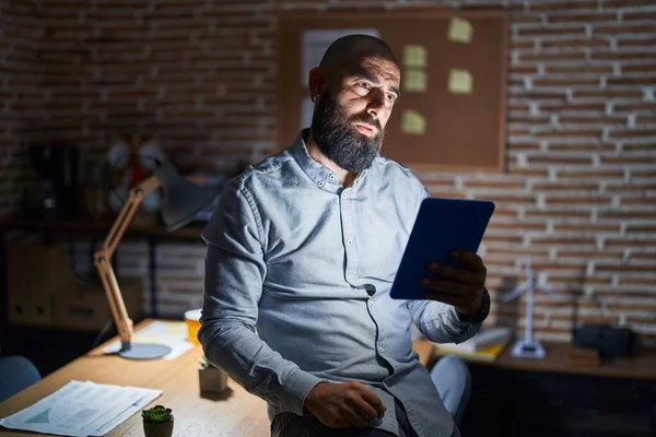 stock image Young hispanic man with beard and tattoos working at the office at night looking sleepy and tired, exhausted for fatigue and hangover, lazy eyes in the morning. 