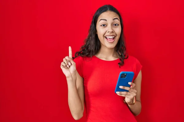 年轻的巴西女人在红色背景下用智能手机指指点点成功的点子 又兴奋又快乐第一大 — 图库照片