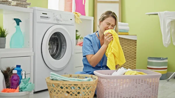 Genç Sarışın Kadın Profesyonel Temizlikçi Çamaşırhanede Kirli Çamaşırların Kokusunu Alıyor — Stok fotoğraf