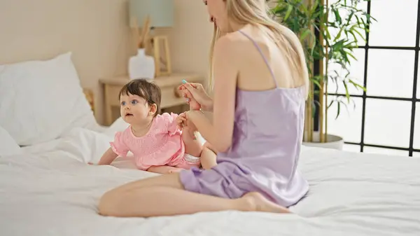 Mother and daughter sitting on bed touching feet at bedroom