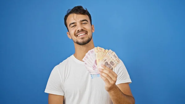 Jonge Latino Man Glimlachen Zelfverzekerd Holding Mexicaanse Peso Geïsoleerde Blauwe — Stockfoto