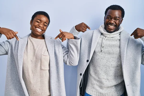stock image Young african american couple standing over blue background together looking confident with smile on face, pointing oneself with fingers proud and happy. 