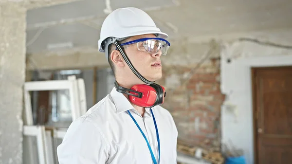 在建筑工地 年轻的惊慌失措的建筑师头戴耳机 表情轻松自在地站着 — 图库照片