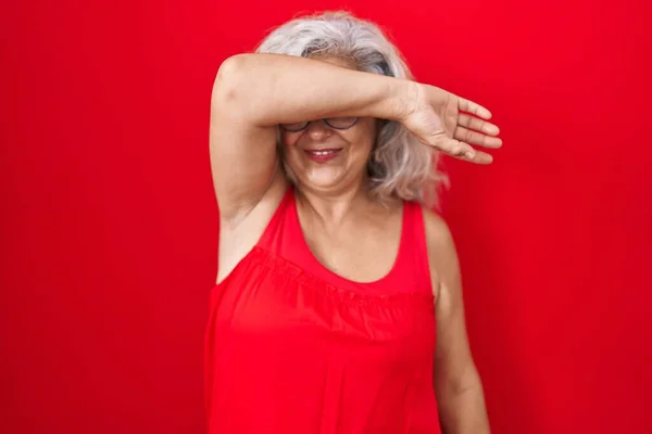 白髪の中年女性が赤い背景の上に立ち 陽気で面白い腕で目を覆います 視覚障害の概念 — ストック写真