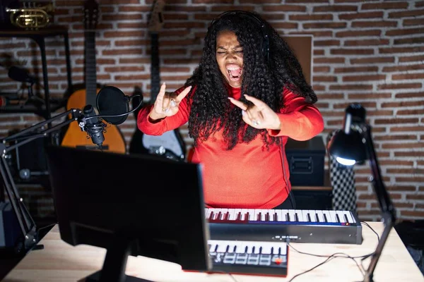 stock image Plus size hispanic woman playing piano at music studio shouting with crazy expression doing rock symbol with hands up. music star. heavy concept. 