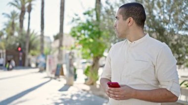Young hispanic man using smartphone at park