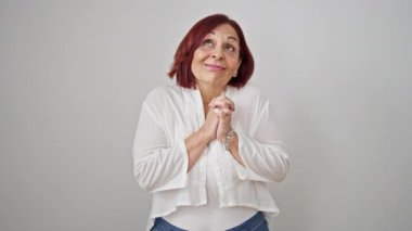 Orta yaşlı bir kadın, elleri kalbimde, soyutlanmış beyaz bir arka planda duruyor.