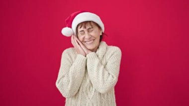 Olgun İspanyol kadın, kendine güvenen, izole kırmızı arka planda noel şapkası takan.