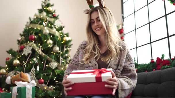 Jong Blond Vrouw Uitpakken Cadeau Zitten Bank Door Kerstboom Thuis — Stockvideo