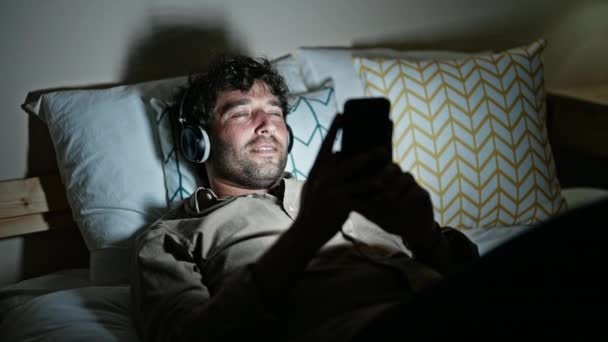 Молодий Іспаномовний Чоловік Слухає Музику Лежить Ліжку Спальні — стокове відео