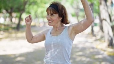 Orta yaşlı kadın parkta spor giyip dans ediyor.
