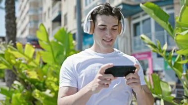 Genç İspanyol adam gülümsüyor. Sokakta akıllı telefondan videolar izliyor.