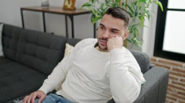 Kanepede oturan genç İspanyol adam evde kollarını rahatça uzatıyor.