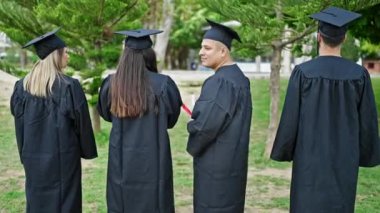 Bir grup öğrenci üniversite kampüsünde el ele selamlaşarak diploma alarak mezun oldular.