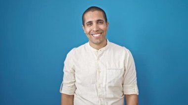 İzole edilmiş mavi arka planda gülümseyen İspanyol genç adam.