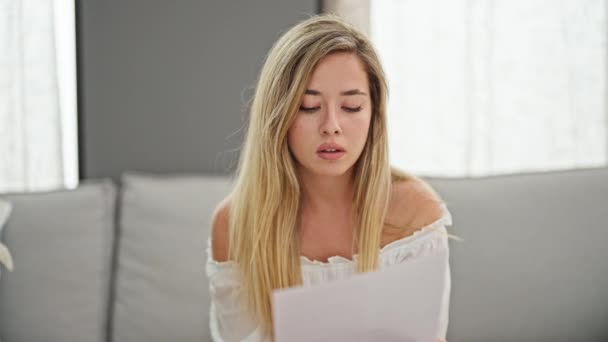 Young Blonde Woman Reading Document Sitting Sofa Home — Stockvideo