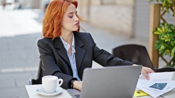 若い赤毛の女性ビジネスワーカーコーヒーショップテラスでコーヒー読書文書を飲む — ストック動画