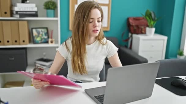 若い金髪女性ビジネスワーカー オフィスでノートパソコンの読書文書を使用して — ストック動画
