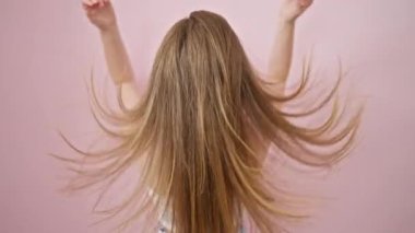 Genç sarışın kadın pembe arka planda saçlarına dokunuyor.