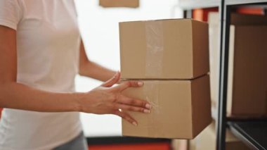 Afrikalı Amerikalı kadın ecommerce işçisi ofiste raflara paket koyuyor.