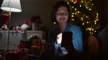 Beyaz kadın akıllı telefon kullanıyor. Evdeki kanepede oturuyor.