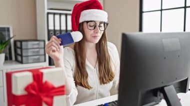 Genç ve güzel İspanyol kadın iş adamı bilgisayar ve kredi kartıyla alışveriş yapıyor. Noel 'i ofiste kutluyorlar.
