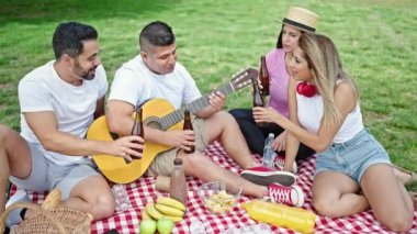 Bir grup insan bir şişe birayla kadeh kaldırıyor parkta piknik yapıyorlar.