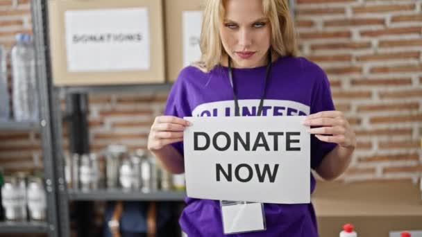Молодая Блондинка Волонтер Улыбается Уверенно Держа Пожертвование Теперь Баннер Благотворительном — стоковое видео