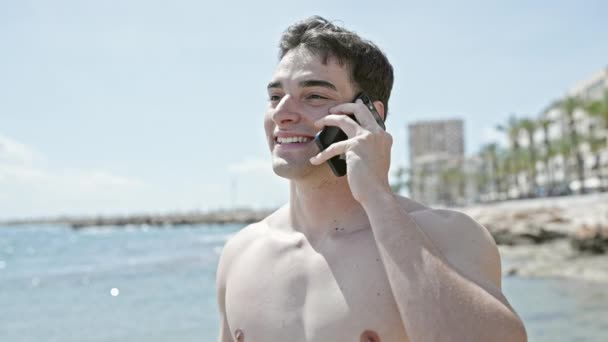 年轻的他的惊慌失措的男人微笑着在海滩用智能手机交谈 — 图库视频影像