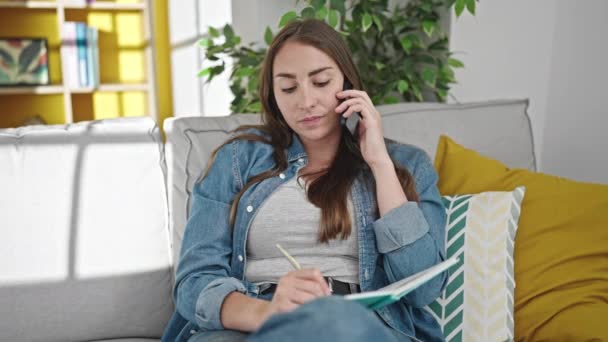 Young Beautiful Hispanic Woman Talking Smartphone Writing Book Home — Stock Video