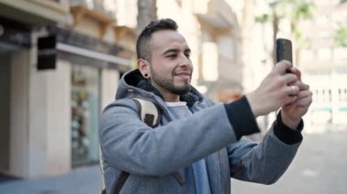 Hispanik adam gülümsüyor. Sokakta akıllı telefonuyla video çekiyor.