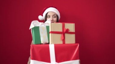 Güzel İspanyol kadın, Noel şapkası takıyor ve kırmızı arka planda hediyeler taşıyor.