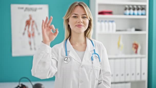 Young Blonde Woman Doctor Smiling Confident Doing Gesture Clinic — Stockvideo