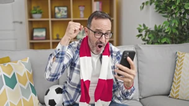 Мужчина Среднего Возраста Поддерживает Футбольную Команду Смотреть Игру Смартфоне Дома — стоковое видео