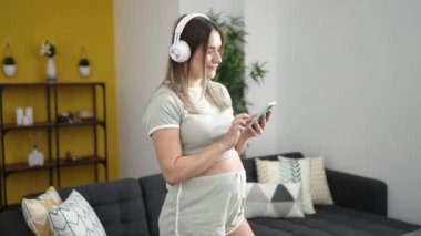 Evde müzik dinleyip dans eden hamile bir kadın.