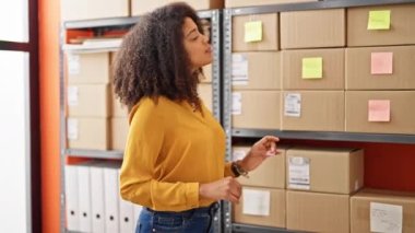Afro-amerikan kadın ecommerce işçisi ofiste gülümseyen bir raf paketi arıyor.