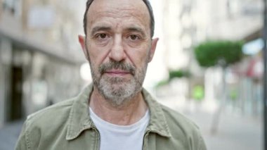 Sokakta ciddi bir ifadeyle duran orta yaşlı bir adam.