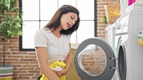 若い白人女性洗濯室でスマートフォンで話す服を洗う — ストック動画