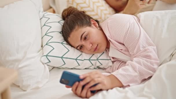 寝室でスマートフォンを使用してベッドに横たわる男女カップル — ストック動画