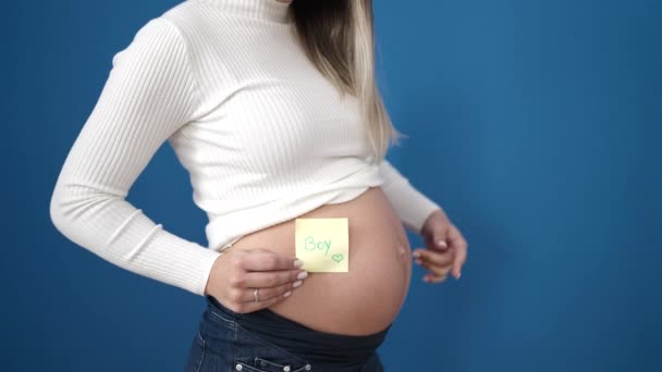 Junge Schwangere Frau Zeigt Auf Knabenmahnpapier Auf Bauch Vor Isoliertem — Stockvideo