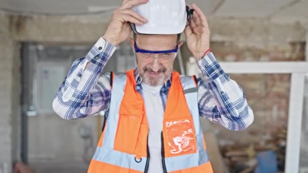 建設現場で自信を持って身に着けているハードハットを笑みを浮かべて中年男性ビルダー — ストック動画