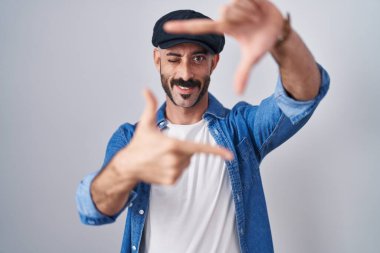Hispanic man with beard standing over isolated background smiling making frame with hands and fingers with happy face. creativity and photography concept. 