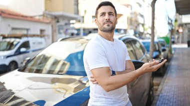 Latin kökenli genç bir adam arabanın yanında duruyor.