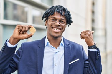 Elinde sanal para olan Afrikalı genç bir adam bitcoin 'i parmağıyla kenarı işaret ediyor ve ağzı açık gülümsüyor. 