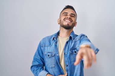 İzole edilmiş arka planda duran genç İspanyol adam sana gülüyor, eli vücudunun üzerinde kamerayı işaret ediyor, utanç ifadesi. 